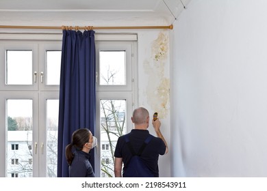 Woman watching a man measuring the temperature of an external wall where mildew is growing with an infrared or laser thermometer.
