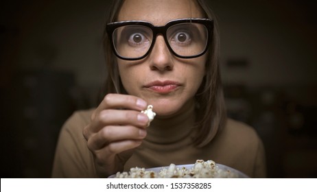 Woman watching movies and eating popcorn, she is addicted and glued to the screen