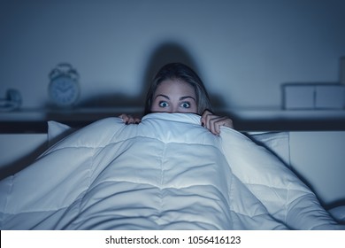 Woman Watching A Scary Horror Movie On Tv Late At Night, She Is Frightened And Hiding Under The Blanket