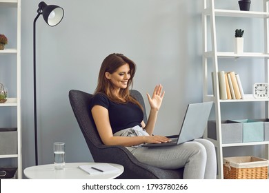 Woman Waving Hand Has Video Call Laptop Computer Online Sitting In Armchair At Home.