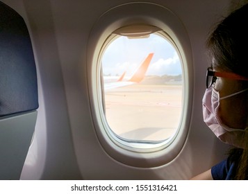 Woman Wear Face Mask Sit On Passenger Economy Seat Near Cabin Window In Airplane. Passenger In Departure Flight Plane At The Airport. Coronavirus Or Covid-19 And Monkeypox Virus Infection Concept. 