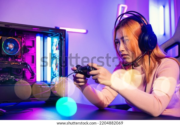 Woman wear gaming headphones playing live stream\
esports games console at home, Gamer using joystick controller for\
virtual tournament plays online video game with computer neon\
lights, Esport concept