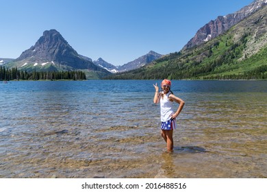 Woman wearing American flag patriotic clothing gives a peace sign at Two Medicine Lake in Glacier National Park