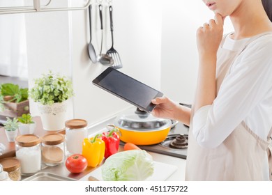 Woman wearing an apron , examine the recipes in the tablet - Shutterstock ID 451175722