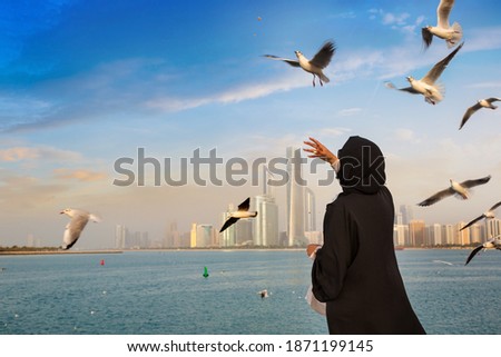 A woman wearing arab clothes is feeding seagulls in Abu Dhabi in a summer day, United Arab Emirates