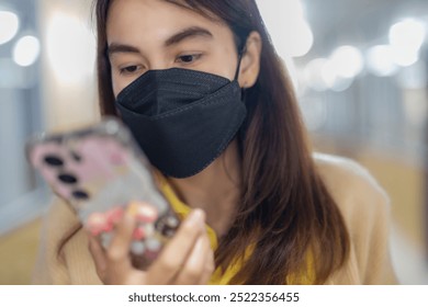 A woman wearing a black face mask, focused on her smartphone, in a well-lit indoor setting, highlighting modern communication, safety, and digital connectivity. - Powered by Shutterstock