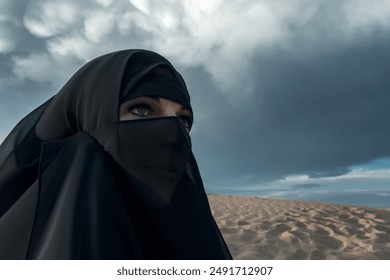 A woman wearing a black niqab looks towards a dramatic stormy sky over desert dunes. Articles on Muslim culture, faith, women's empowerment, or the intersection of tradition and nature.