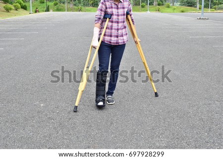A woman wearing a black plaster cast right foot with crutches and is walking on the street.