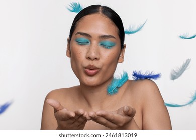 Woman wearing blue makeup blowing on blue feathers