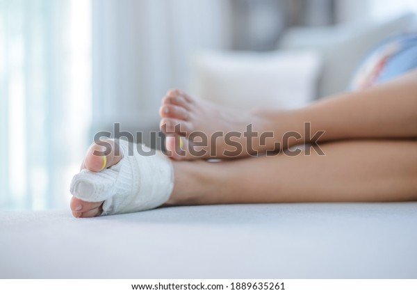 Woman wearing blue pajamas bone fracture foot and\
leg on female patient with splint cast and crutches during surgery\
rehabilitation and orthopaedic recovery lying on couch staying at\
home.