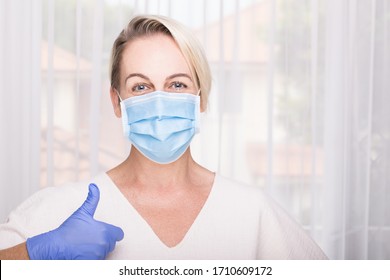 Woman Wearing Blue Surgical Mask And Latex Gloves Giving Thumbs Up. Hospital Environment. Healthcare Concept.