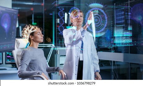 Woman Wearing Brainwave Scanning Headset Sits in a Chair while Scientist Using Futuristic Holografic Interface. In the Modern Brain Study Laboratory Monitors Show EEG Reading and Brain Model.