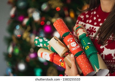 Woman Wearing A Christmas Sweater Holding Some Christmas Cracker On A Lighted Christmas Tree.