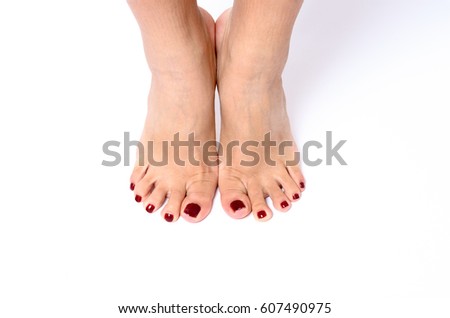 Woman wearing colorful modern red nail varnish on her toenails after a beauty treatment and pedicure at a spa standing on tiptoe showing off her feet over a white background