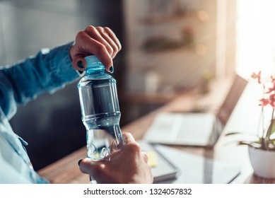 Woman wearing denim shirt working in the office and opening plastic bottle of water
