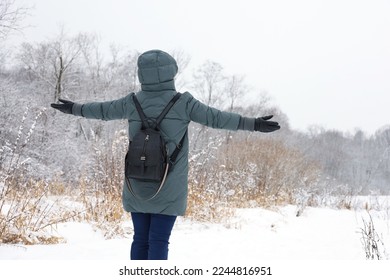 Woman wearing down jacket standing with her hands spread out to the sides and enjoying the snowy weather. Leisure in winter park, cold season