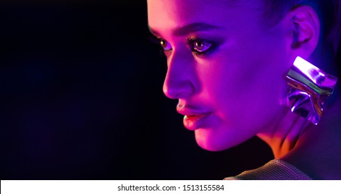 Woman wearing earrings in colorful bright neon lights, posing in studio, free space