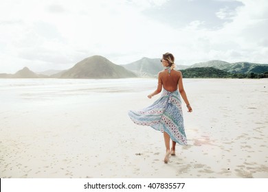 Woman wearing ethnic flying dress walking barefoot at the beach, Lombok, Indonesia