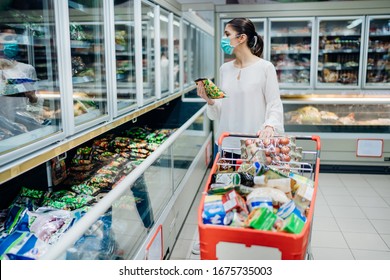Woman wearing face mask buying in supermarket.Panic shopping during Coronavirus covid-19 pandemic.Budget buying at a supply store.Buying freezer smart purchased household pantry groceries - Shutterstock ID 1675735003