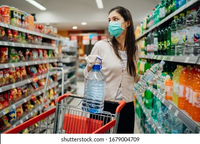 Woman wearing face mask buying bottled water in supermarket/drugstore with sold-out supplies.Prepper buying bulk supplies due to Covid-19 or Coronavirus and panic buying concept.