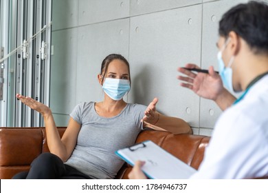 Woman Wearing Face Mask Sitting On The Sofa And Talking To The Professional Psychologist While Wearing Face Mask Conducting A Consultation And Making Notes During Coronavirus Or COVID 19 Outbreak