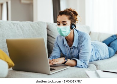 Woman Wearing Face Mask And Surfing The Net On Laptop While Relaxing In The Living Room.