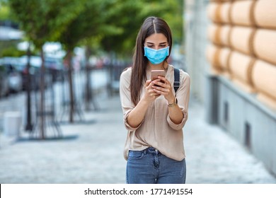 Woman Wearing Face Mask While Text Messaging On Mobile Phone At City Street. Woman Outdoors Wearing A Facemask While Texting On Her Cell Phone. 