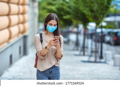 Woman Wearing Face Mask While Text Messaging On Mobile Phone At City Street. Woman Outdoors Wearing A Facemask While Texting On Her Cell Phone. 