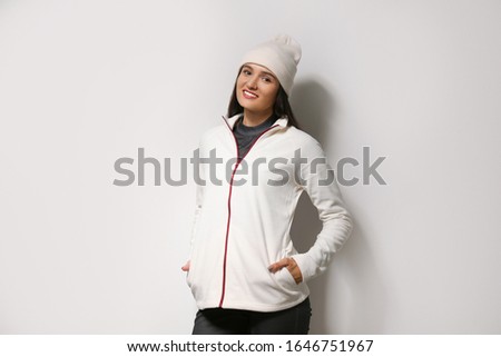 Woman wearing fleece jacket and hat on light grey background. Winter sport clothes