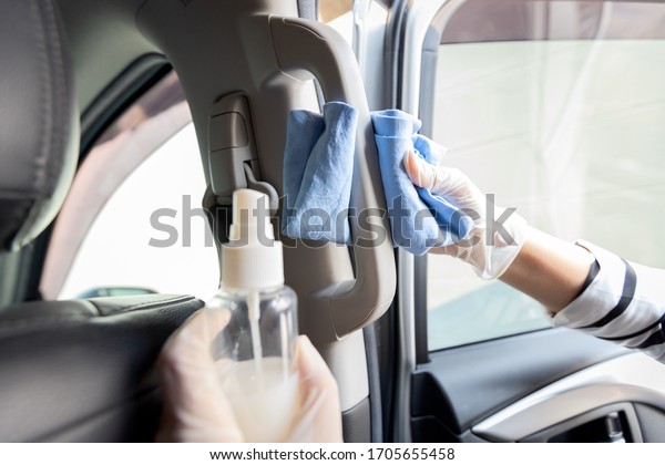 Woman wearing glove,girl with alcohol antiseptic or\
spray bottle disinfecting in hand,cleaning on car handle,interior\
in car,during Coronavirus pandemic,Covid-19,wipe the dirty surface\
inside the car