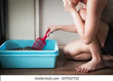 Woman wearing a gray spaghetti strap cleaning the blue little box or cat toilet, feeling stinky