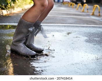 Woman Wearing Grey Polka Dots Rain Boots Jumping Into A Puddle. Close Up