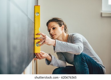 Woman wearing grey shirt using leveling tool at home - Powered by Shutterstock