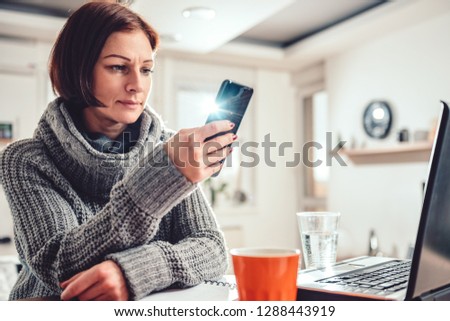 Woman wearing grey sweater using smart phone in the office