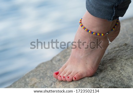 Woman is wearing handmade anklet, in a natural environment, in a bank of river. 