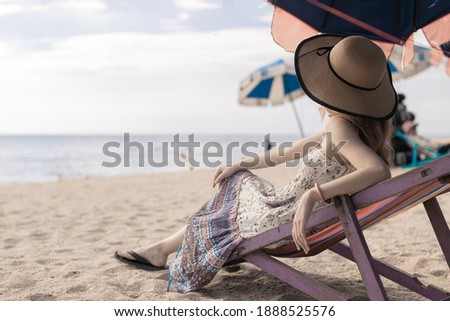 woman wearing hat on deckchair at the beach look at the sea