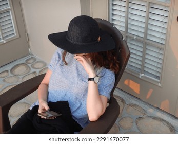 Woman wearing a hat, sitting on a deck looking at her phone