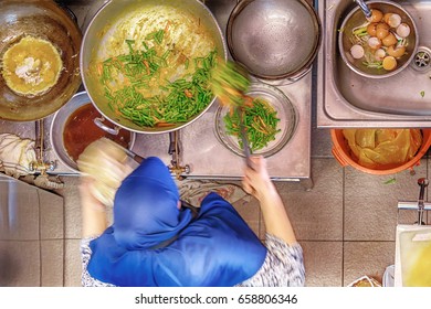 Woman Wearing Head Scarf Cooks Malay Food In Hawker Food Stall In Little India, Singapore.