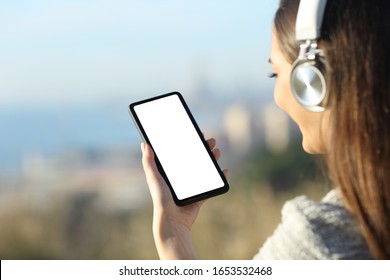 Woman wearing headphones showing and using blank phone screen outdoors