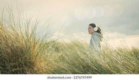 woman wearing headphones walking through long grass wearing a hoodie. Getting away from it all concept. - Powered by Shutterstock