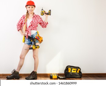 Woman Wearing Helmet Using Drill. Girl Working At Flat Remodeling. Building, Repair And Renovation.