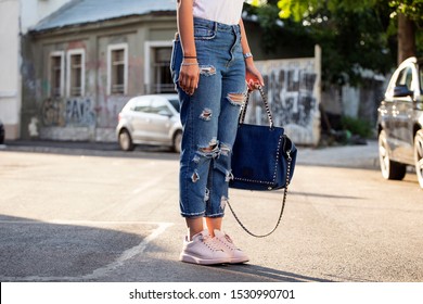 Woman wearing high waist ripped jeans, white tshirt and denim purse, posing at sunset, street background