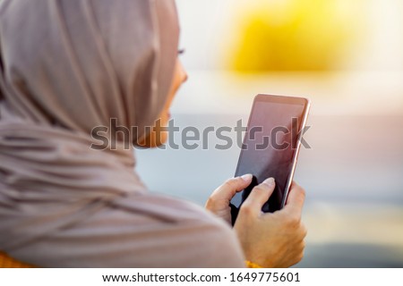 Woman wearing hijab browsing internet on mobile phone outdoors. Modern arabian girl using mobile phone on the street. Close up of beautiful woman wearing hijab smiling while texting on mobilephone