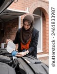 Woman wearing hijab filling water tank in car engine