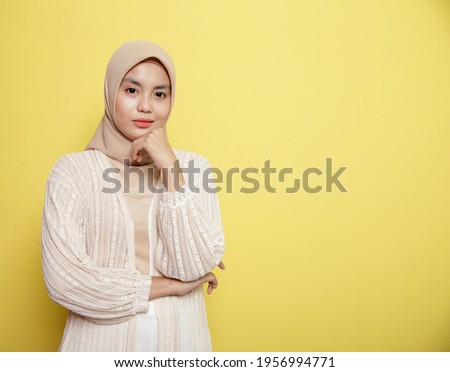 woman wearing hijab smiling while holding her jaw looking at the camera isolated on a yellow background