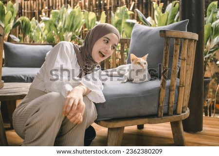 A woman wearing a hijab tries to tease the cat beside her