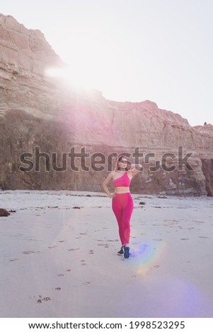 Woman wearing hot pink gym clothes exercising at the beach.