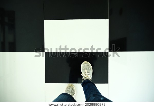 A\
woman wearing jeans and sneakers stepped on a tiled floor that was\
evenly divided into black and white. The concept of color is\
different with opposite meanings. shiny tiled\
floor