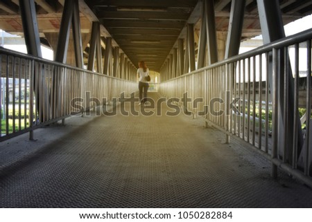 A woman wearing jeans and a T-shirt with a suitcase walks on a stretched bridge.