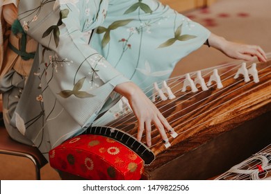 A woman wearing kimono is playing a traditional Japanese musical instrument  Koto, a Japanese harp.